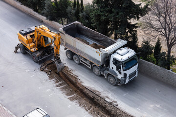Road construction crew working on street repair with machinery and a dump truck