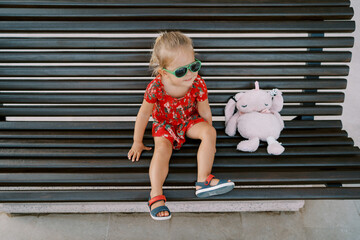 Little girl sitting on a wooden bench with a pink plush rabbit