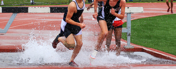 Runners Compete in a Steeplechase Race Splashing Through Water Obstacles During a Track Event