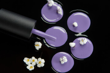 Fototapeta premium Open black nail polish bottle with a brush dripping lavender polish onto a dark surface with small flower accents