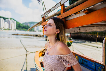 Caucasian woman model with blue eyes looking forward beach in the background, boats near 