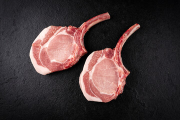 Raw dry aged trimmed bone-in pork loin chops cutlets offered as top view on a black board