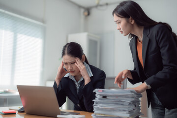 Overworked Asian businesswoman experiencing headache and stress from excessive workload, facing criticism from her manager in a high-pressure office environment filled with deadlines and paperwork