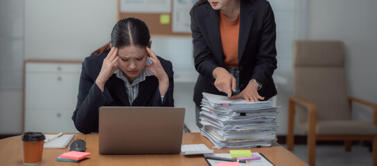 Asian businesswomen are stressed from being blamed by their bosses for working with a computer at the office desk and having a large pile of unfinished paperwork © MINAE