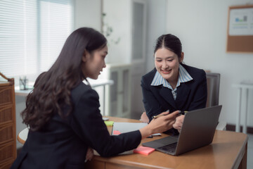 Obraz premium Two asian businesswomen discussing working together using laptop in office, smiling and happily brainstorming and planning project, working and sharing ideas