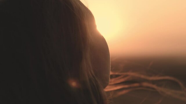 girl prays looking at sunset, long hair is flying away in glare of sunlight rays in strong wind, looking at dawn, lonely hike of brave girl, looking into sky with her eyes, believing good.