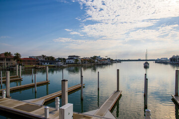 Obraz premium A gorgeous landscape with ocean water, homes and boats on the water, blue sky and clouds, lush green palm trees at sunrise in Clearwater Florida USA