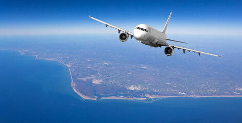 White passenger airplane flying over coastal area on sunny day