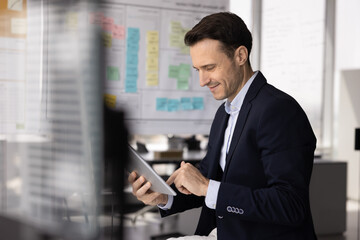 Positive satisfied Latin business leader man working with tablet computer in office, typing on...