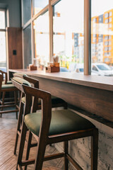 Cozy modern cafe interior with wooden chairs and high counter along the window. Warm sunlight creates a welcoming atmosphere. Minimalist design with natural wood and neutral tones