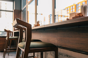 Cozy modern cafe interior with wooden chairs and high counter along the window. Warm sunlight creates a welcoming atmosphere. Minimalist design with natural wood and neutral tones