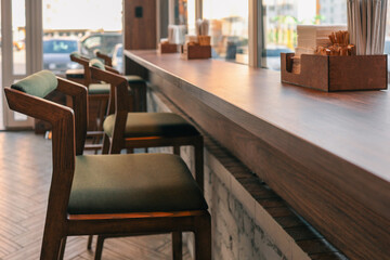 Cozy modern cafe interior with wooden chairs and high counter along the window. Warm sunlight creates a welcoming atmosphere. Minimalist design with natural wood and neutral tones