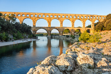 Pont du Gard, ancient Roman aqueduct bridge, Provence late afternoon golden light on arches mirroring in river, Gorges du Gardon, natural landscape designated Biosphere Reserve by UNESCO, France