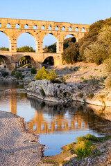 Pont du Gard, ancient Roman aqueduct bridge, Provence late afternoon golden light on arches mirroring in river, Gorges du Gardon, natural landscape designated Biosphere Reserve by UNESCO, France