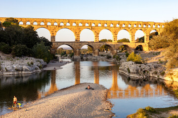 Pont du Gard, ancient Roman aqueduct bridge, Provence late afternoon golden light on arches mirroring in river, Gorges du Gardon, natural landscape designated Biosphere Reserve by UNESCO, France
