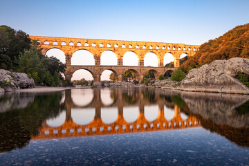 Pont du Gard, ancient Roman aqueduct bridge, Provence sunset light on arches mirroring in river, Gorges du Gardon, natural landscape designated Biosphere Reserve by UNESCO, France