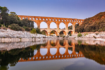 Pont du Gard, ancient Roman aqueduct bridge, Provence sunset light on arches mirroring in river, Gorges du Gardon, natural landscape designated Biosphere Reserve by UNESCO, France