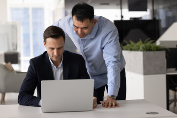 Two professional colleagues watching new application, software work, meeting at laptop, using computer. Project manager showing online product to coworker, asking for advice
