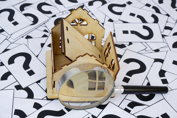 Damaged house under magnifying glass on question marks. Cost for house repair concept.