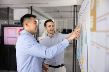 Successful multiethnic businessmen making business model canvas board with sticky notes, discussing teamwork group management, planning schedule, tasks, brainstorming on strategy