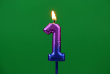 Burning pink and blue birthday candle on green background, number 1