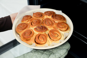 Woman taking delicious cinnamon rolls out of oven, closeup