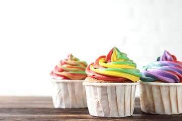 Delicious cupcakes with colorful cream on wooden table against white background, closeup. Space for text