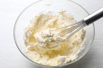 Bowl with whisk and whipped cream on white wooden table, closeup