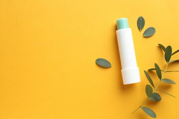 Lip balm and eucalyptus leaves on yellow background, flat lay. Space for text