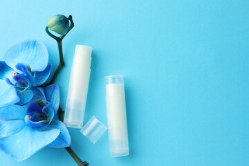 Lip balms and orchid flowers on light blue background, flat lay. Space for text