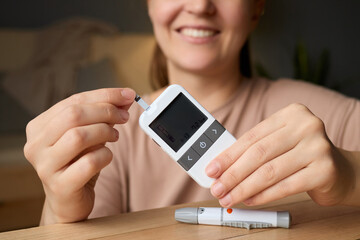 A woman holds a glucometer with a test strip while demonstrating how to check blood sugar levels. Soft lighting creates a warm and inviting atmosphere