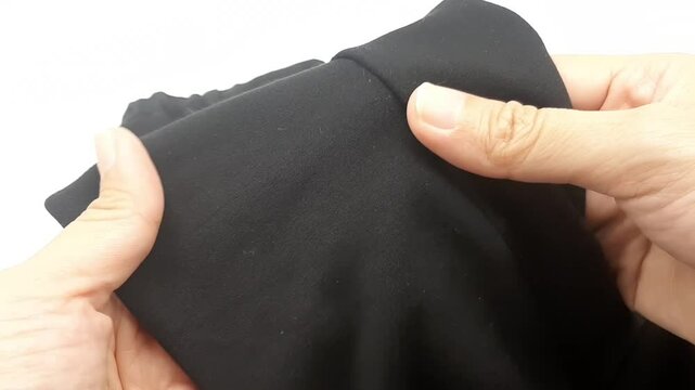 Two hands holding and stretching a rather slippery black cloth that is the fabric from the pants.