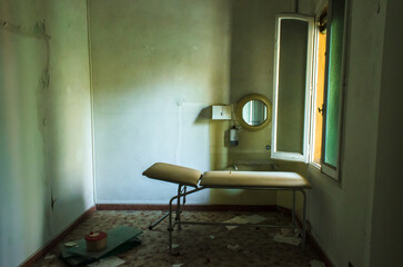 Una sala dell&rsquo;ospedale abbandonato del Lido di Venezia con una barella e un piccolo specchio rotondo illuminati dalla luce che entra da una finestra aperta