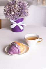 Cup of tea and berry croissant, bouquet of violet flowers
