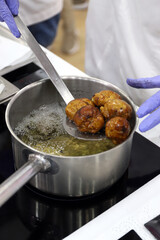 chef cocinando buñuelos gourmet en una olla con aceite muy caliente en la cocina y dándoles la vuelta con una cuchara de acero inoxidable