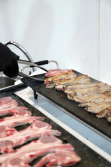 chef friendo a la plancha chuletas de cordero y dándoles la vuelta con pinas de cocina