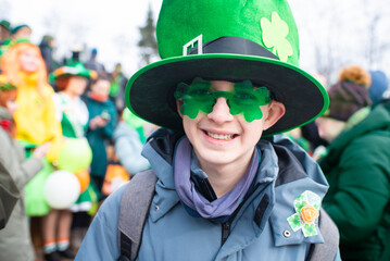 Portrait of a 12 year old boy wearing a green hat and shamrock glasses on St. Patrick's Day.