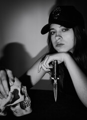 A pretty girl in a black cap with a stiletto in her hand. Black and white art photo.