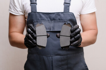 Close-up of man wearing overalls holding two brake pads in hands while standing in workroom or garage. Brake pad replacement concept, car serviceability © GRON777