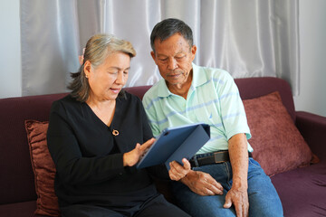 Elderly and technology concept. A portrait of happy senior asian couple communicating via internet and wireless technology with family and friends after retiring and just resting at home sweet home.