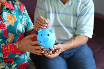 Saving money investment for future. Senior asian man hands putting money coin in piggy bank. Old...