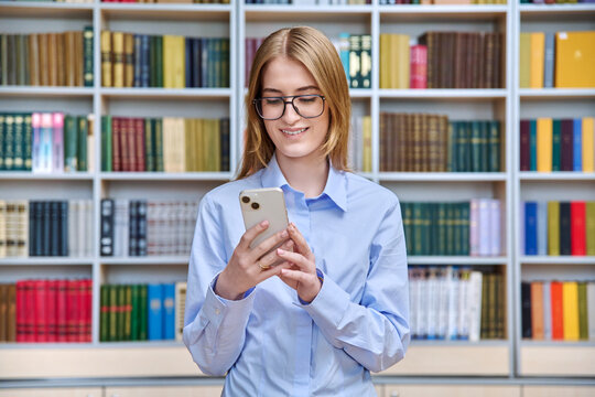 Teen girl college student with smartphone inside library classroom - Powered by Adobe