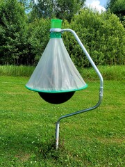 Horsefly trap against green trees. Photo of black ball insect trap on stand in mown meadow. Agricultural equipment for insect protection.