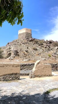 Traditional emirati architecture is showcased in the al bithnah fort, perched atop a rocky hill, with a foreground featuring a partially ruined wall and a paved pathway