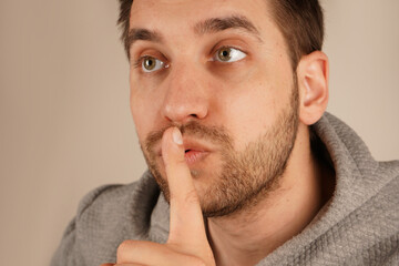 Fototapeta premium With an index finger pressed to his lips, the man requests silence in a calm manner. His composed expression enhances the effectiveness of the gesture. The image communicates tranquility and order.
