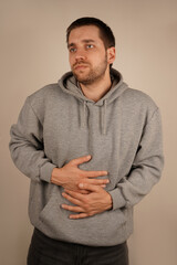 A young man is bending forward, pressing his hands against his stomach, overwhelmed by pain. The...