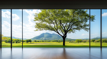 Expansive view of a green landscape through large windows framed by a vibrant tree and rolling hills on a sunny day