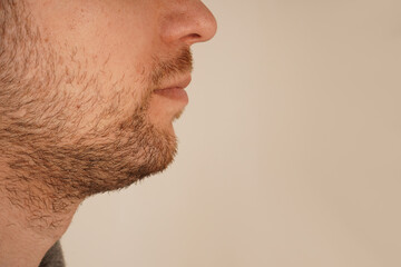 Fototapeta premium A detailed close-up of a man's chin with subtle stubble, showcasing masculine appeal. The unshaven look exudes effortless charm and simplicity. Perfect for themes of grooming and casual style.