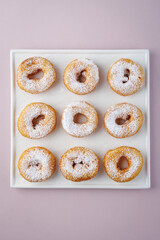 Donuts with powdered sugar on a light plate and a delicate purple background. Top view