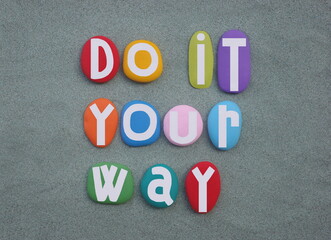 Do it your way, creative slogan composed with multi colored hand painted stone letters over green...